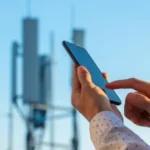 Smartphone recebendo sinal de 5G Broadcast de uma torre, com ícones de canais de TV ao fundo