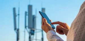 Smartphone recebendo sinal de 5G Broadcast de uma torre, com ícones de canais de TV ao fundo