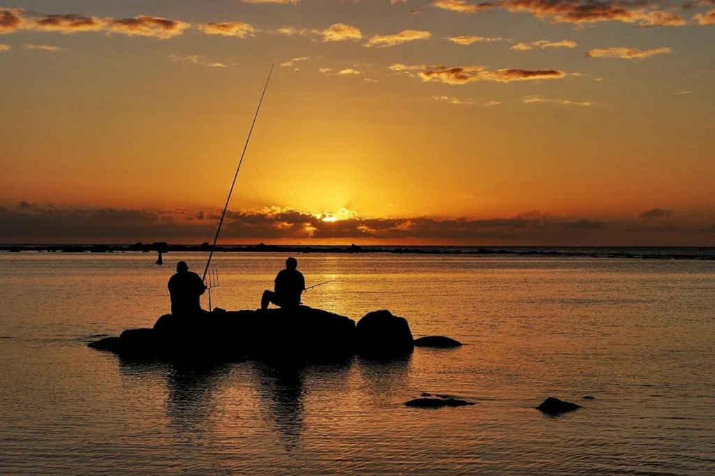 Pescadores no pôr do sol na Ilha Maurício, refletindo na água tranquila